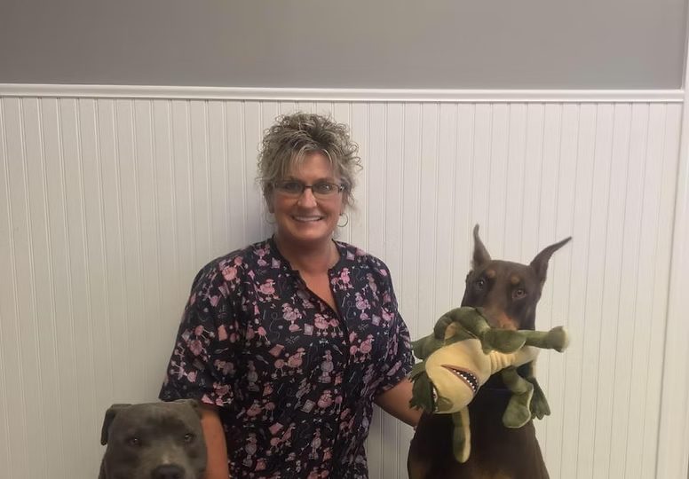 A Double K team member smiling between two happy dogs holding a toy